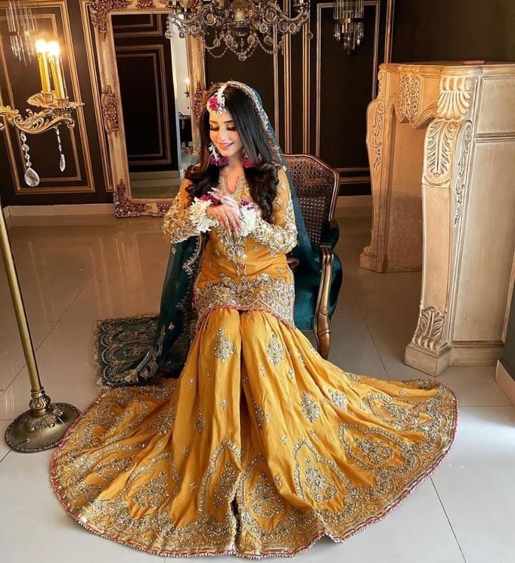 a woman in a yellow and gold wedding dress sitting on a chair with a chandelier