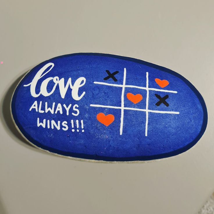 a painted rock that says love always wins with hearts and crosses drawn on it's surface