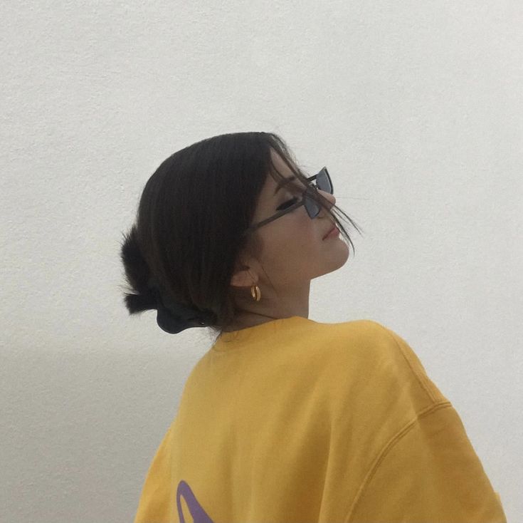 a woman wearing glasses and a yellow shirt looks off into the distance with her hair in a bun