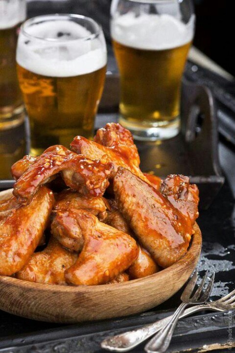 a wooden bowl filled with chicken wings next to glasses of beer