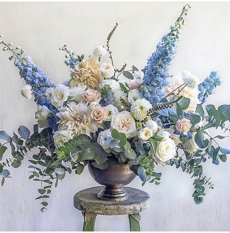 a vase filled with lots of flowers sitting on top of a wooden stool next to a wall