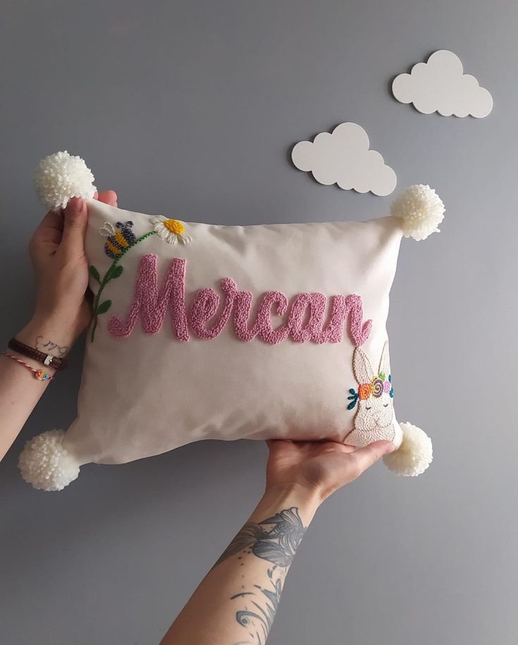 someone holding a pillow with the word mersey on it and pom - poms