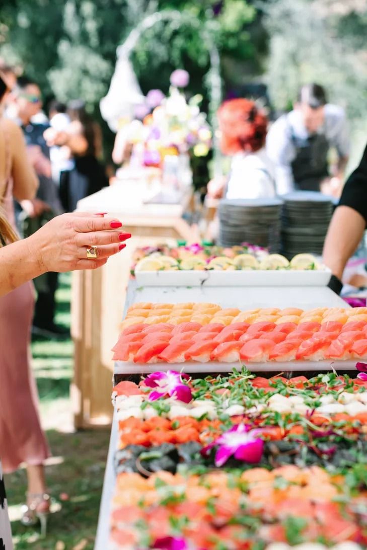 a woman standing in front of a table filled with different types of sushi and other foods