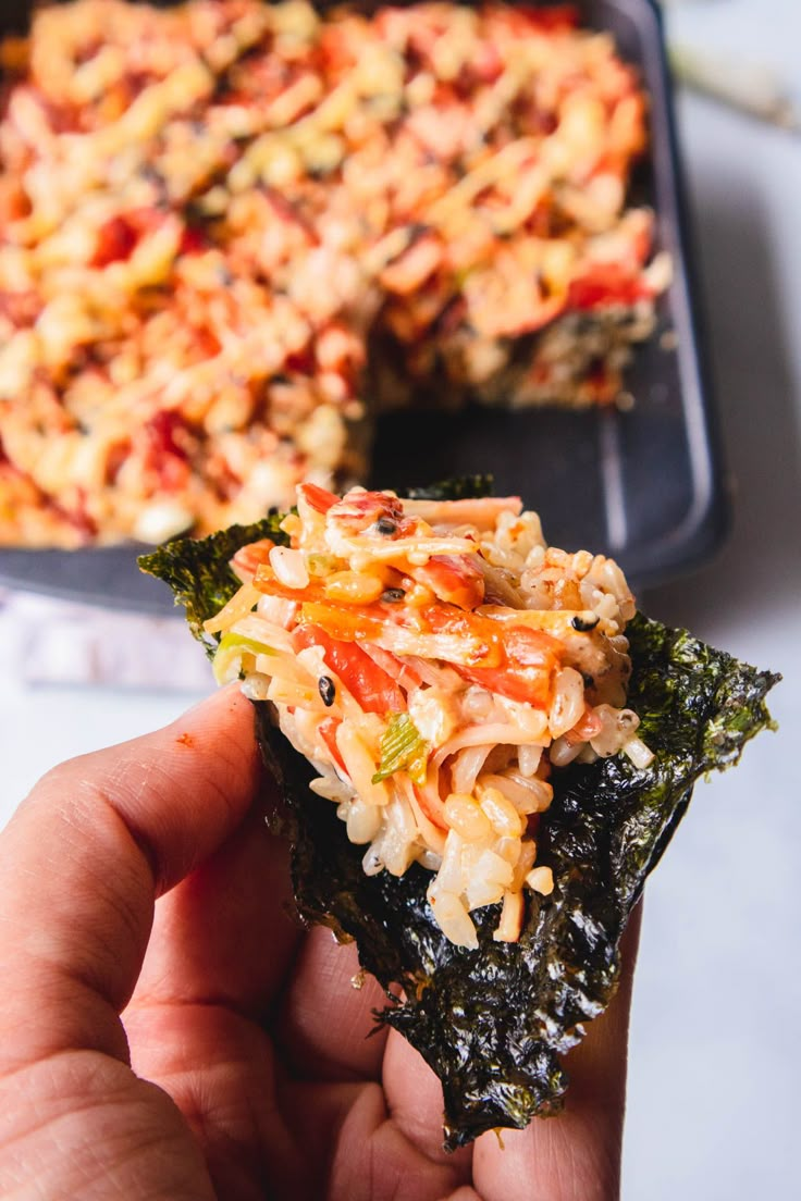 someone holding up a piece of food in front of a casserole dish on a table