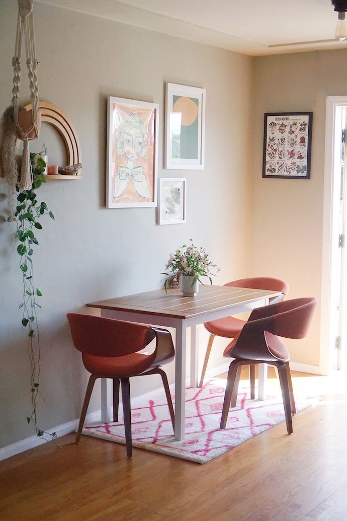 a dining room table with two chairs and pictures on the wall above it in front of a door