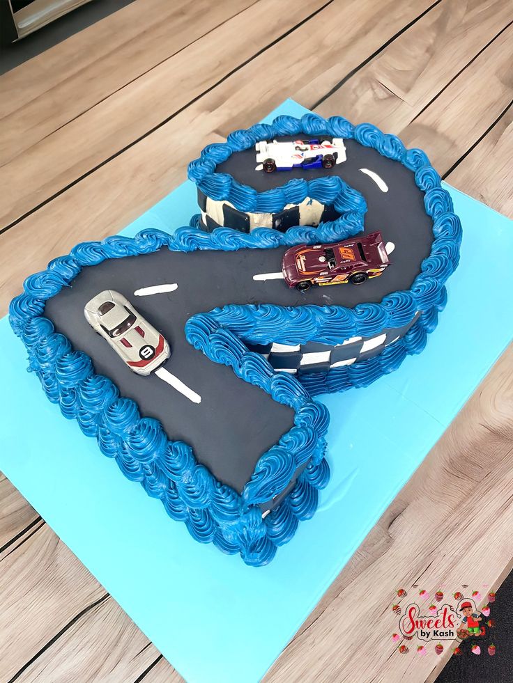 a birthday cake shaped like the letter s with cars on it sitting on top of a table