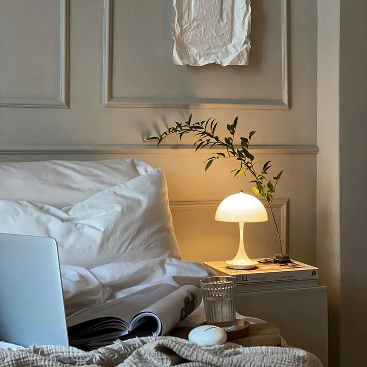 a laptop computer sitting on top of a bed next to a lamp and a plant