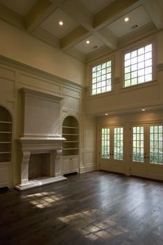 an empty living room with wood floors and large windows on either side of the fireplace