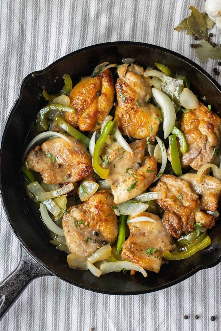 a skillet filled with chicken and onions on top of a striped table cloth next to flowers