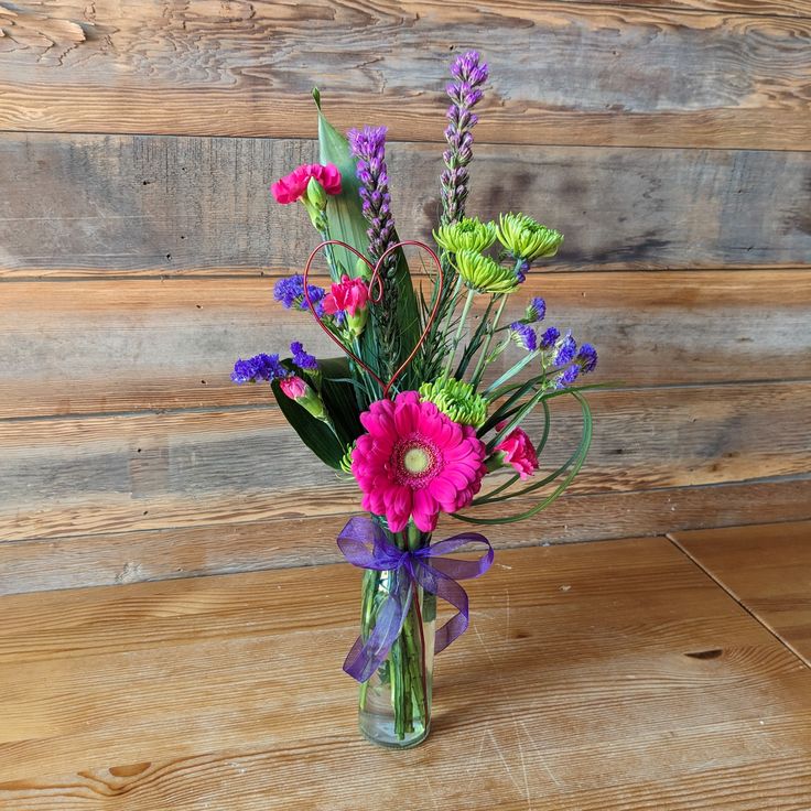 a vase filled with purple and green flowers on top of a wooden table next to a wall