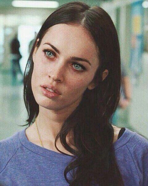 a woman with long black hair and blue eyes looks at the camera while standing in an airport