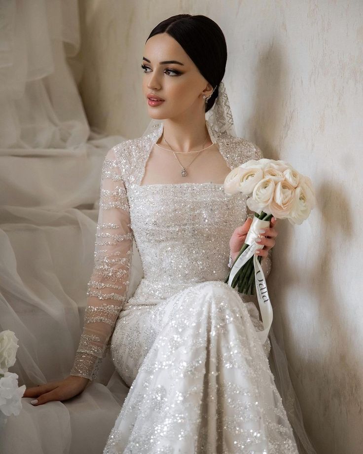 a woman in a wedding dress sitting on a chair holding a bridal bouquet and posing for the camera