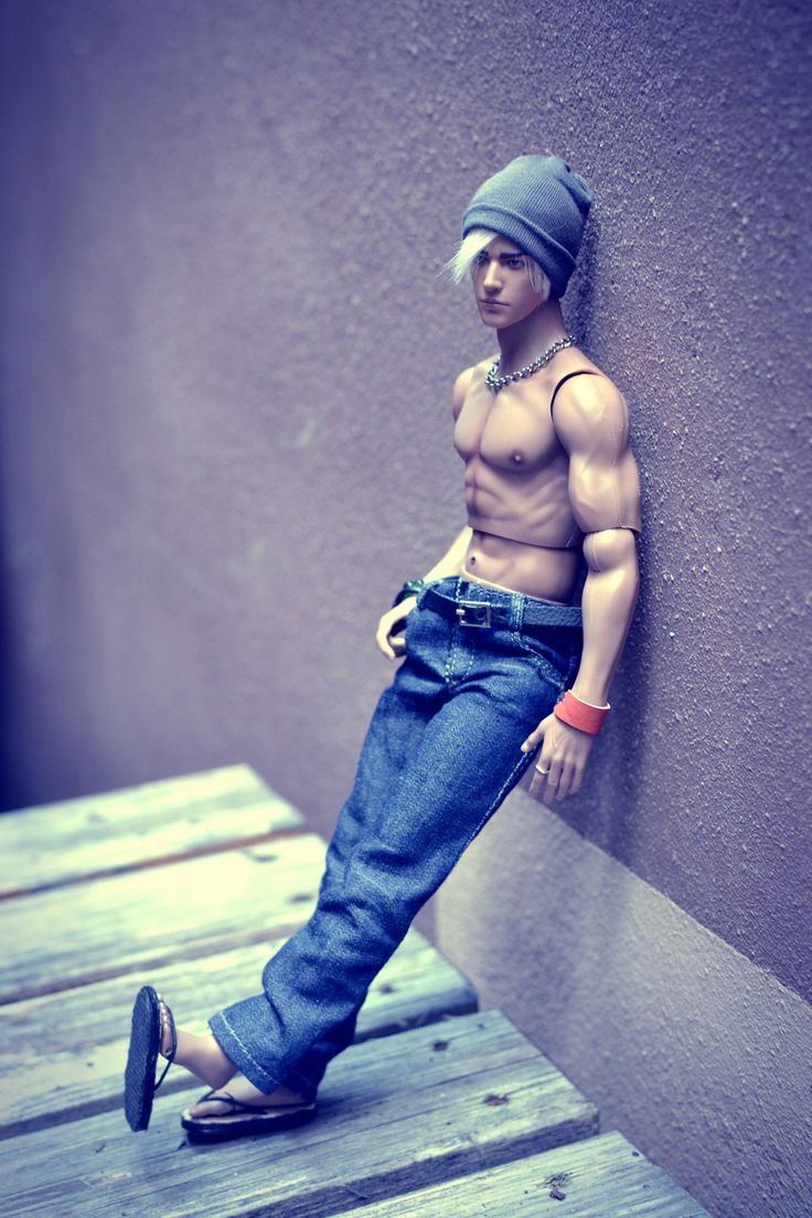 a man with no shirt standing next to a wall wearing jeans and a beanie