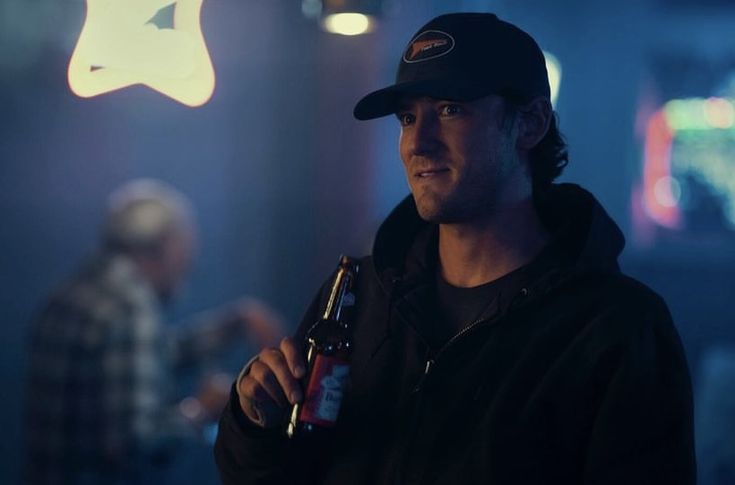 a man holding a beer bottle in his right hand and wearing a black baseball cap