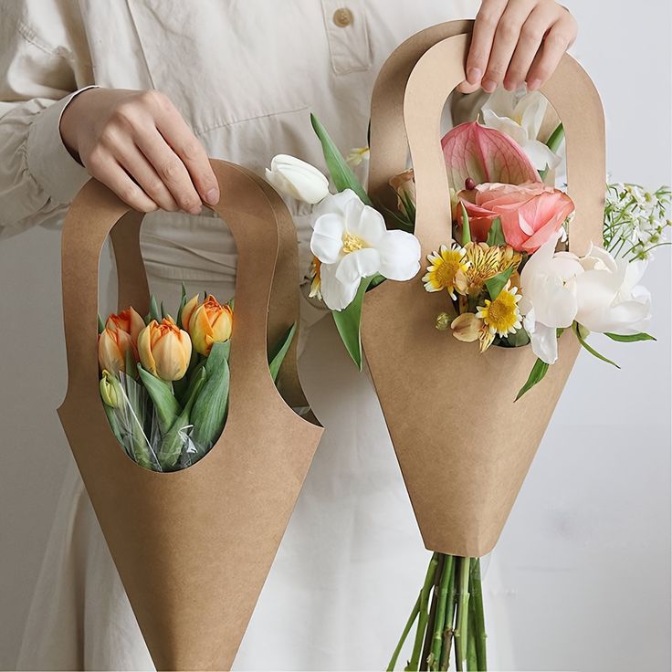 a person holding two brown paper bags with flowers in them