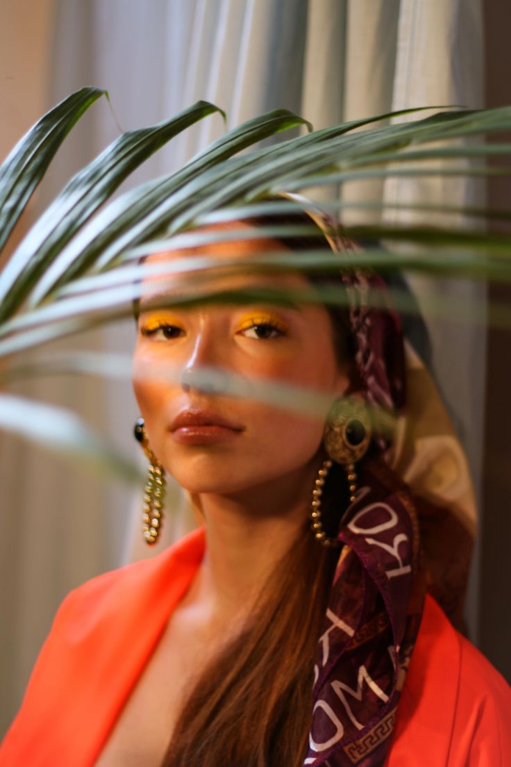 a woman in an orange dress is wearing large earrings and a scarf around her head