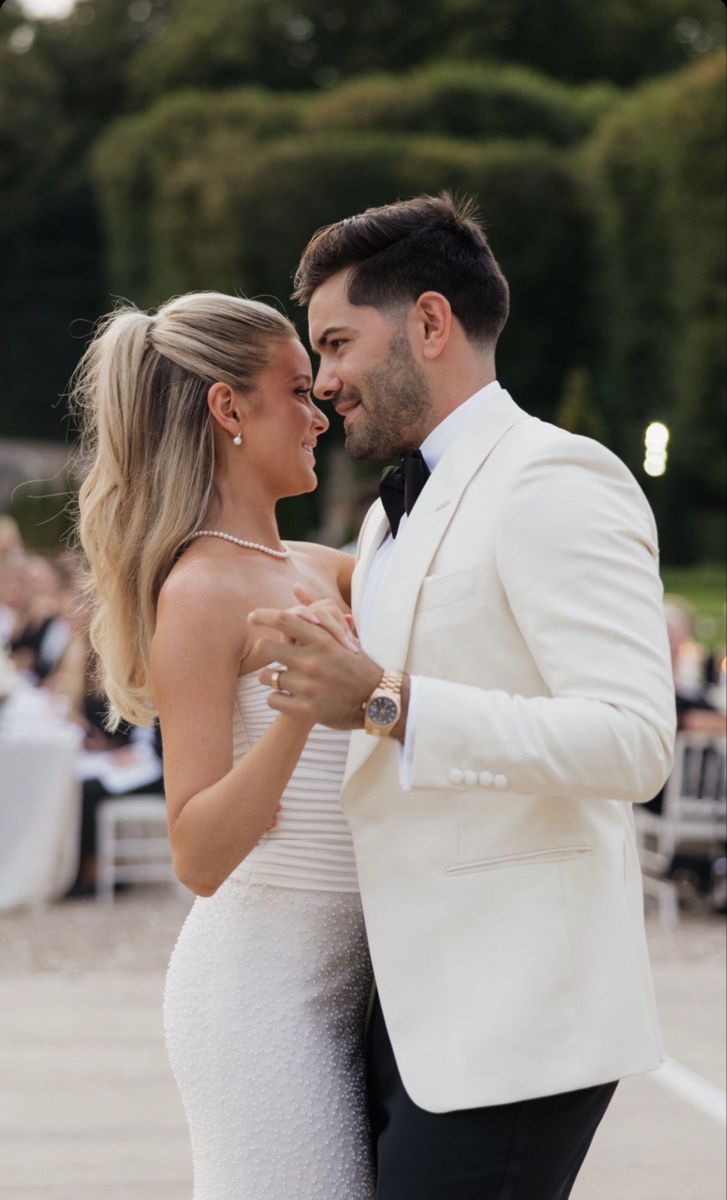 a bride and groom dancing together at their wedding reception in an outdoor setting with people sitting around the tables