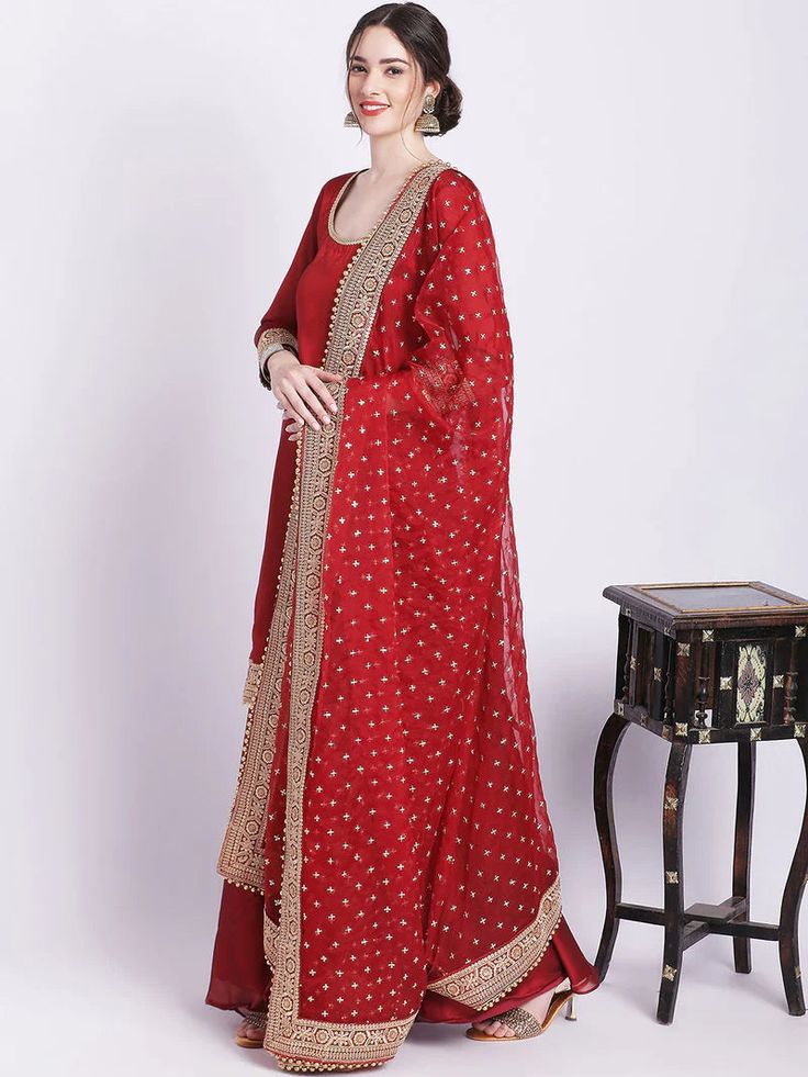 Experience exclusive, elevated luxury wearing our maroon silk palazzo set with organza dupatta. Adorned with intricate zari and sequin work, our regal piece captures timeless sophistication with its rich hues, silken textures, and ornate detailing. Exuding an aura of refined elegance, treat yourself to an extraordinary yet understated look. No. of pieces - 3 piece set. Fabric - Silk and Organza. Color - Maroon. Kurta Length - 42 inches. Washing Instructions - Dry Clean. Designer Organza Palazzo Set For Navratri, Elegant Red Unstitched Suit For Festive Occasions, Elegant Red Unstitched Suit For Festive Season, Floor-length Gold Palazzo Set With Dupatta, Navratri Organza Palazzo Set With Straight Kurta, Floor-length Chanderi Palazzo Set With Gota Work, Anarkali Organza Palazzo Set With Dupatta, Chanderi Palazzo Set With Gota Work, Floor-length, Anarkali Palazzo Set With Organza Dupatta