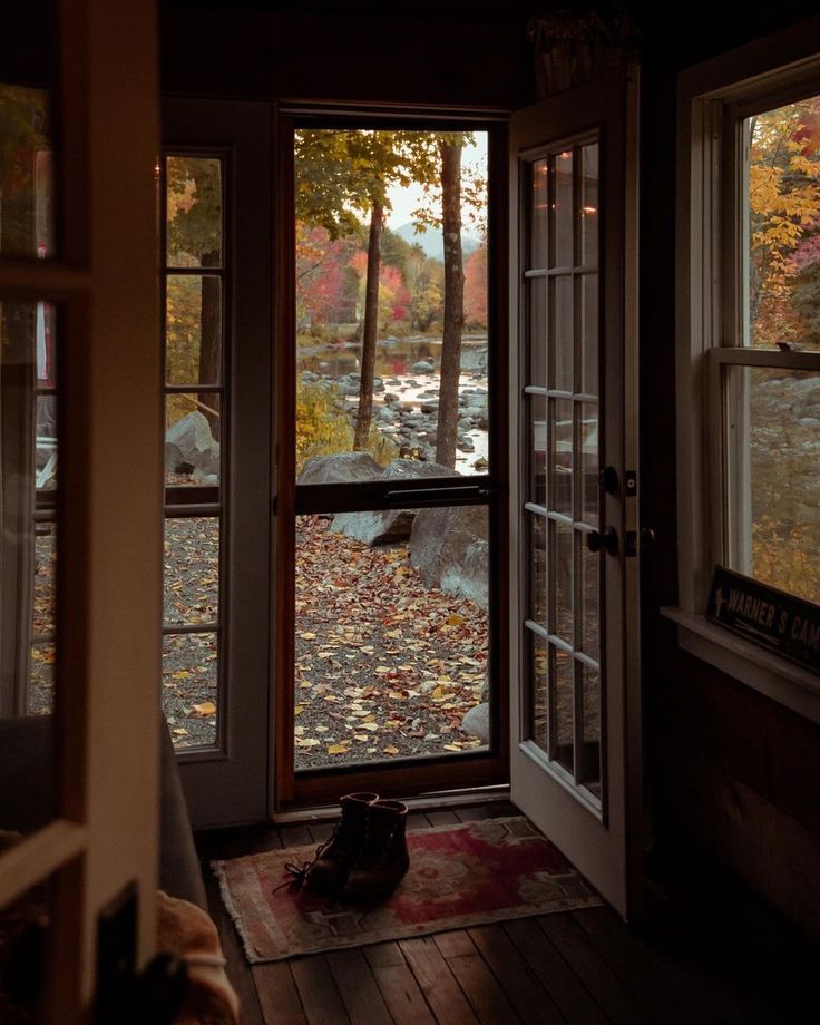 an open door leading into a room with lots of leaves on the floor and trees outside