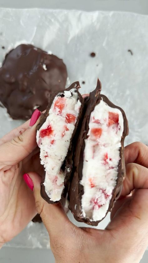 two hands holding chocolate covered pastries with whipped cream and strawberries on them,