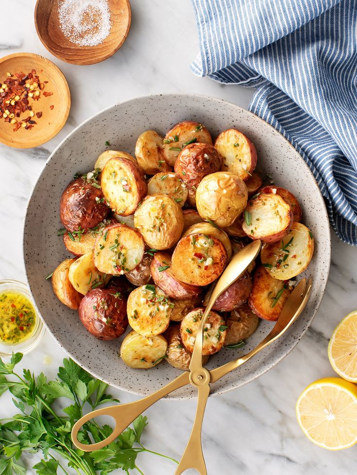 a bowl filled with potatoes and garnished with seasoning next to sliced lemons