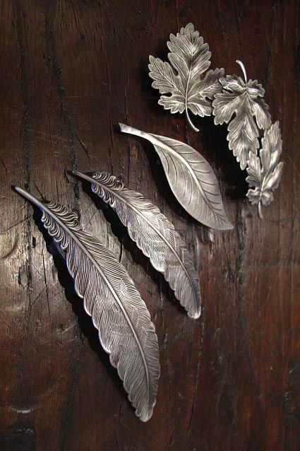 three silver leaf brooches sitting on top of a wooden table