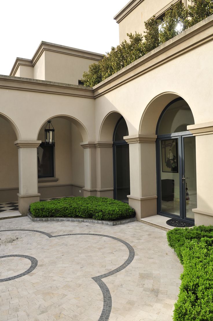 an outdoor courtyard with circular hedges and stone walkways, surrounded by white stucco walls