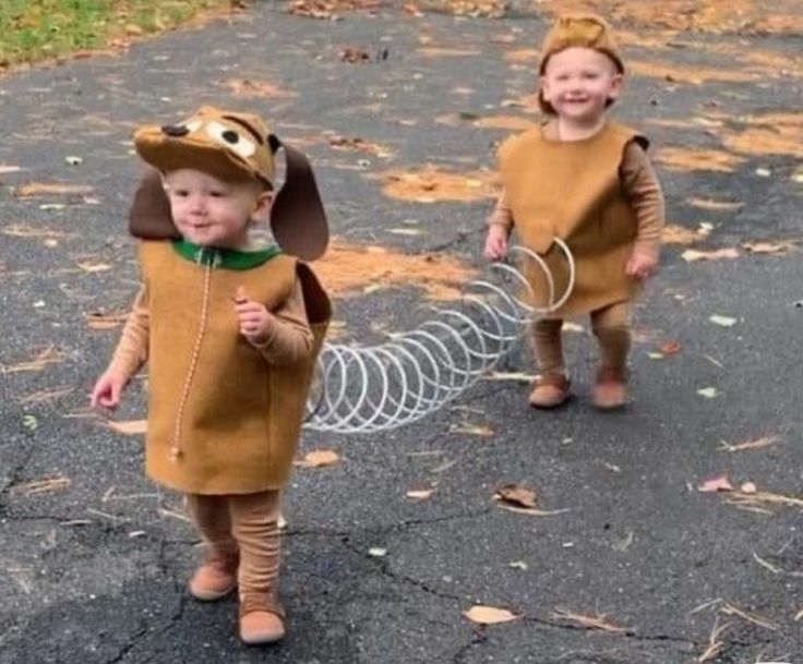 two young children dressed in costumes walking down the street with a dog on it's leash