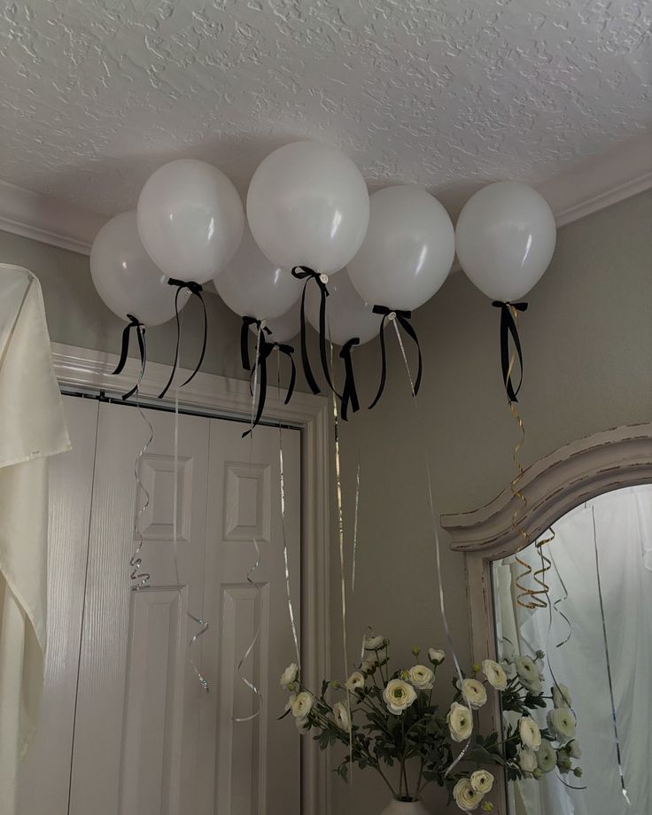 white balloons are hanging from the ceiling above a vase with flowers and streamers in front of a mirror