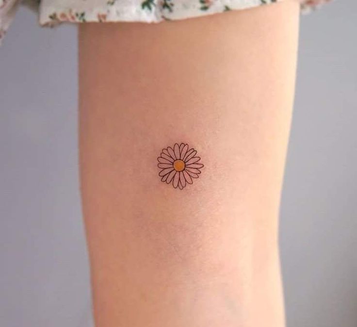 a small flower tattoo on the ankle is shown in this image, it looks like an orange and yellow daisy