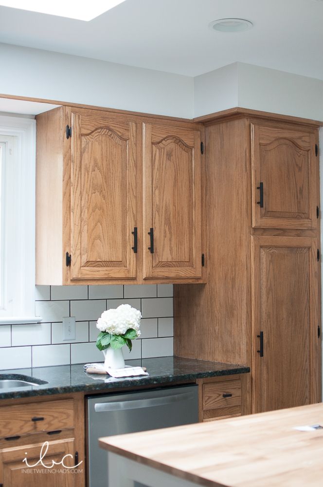 a kitchen with wooden cabinets and black counter tops, white flowers in a vase on the sink