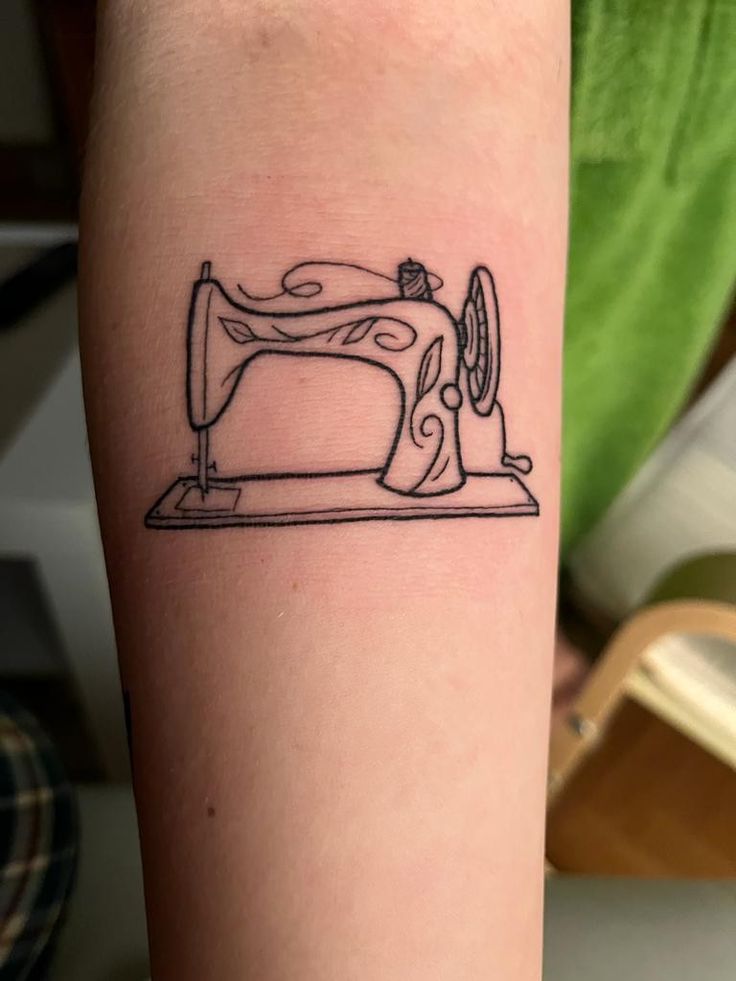 a tattoo on the arm of a woman with a sewing machine in front of her