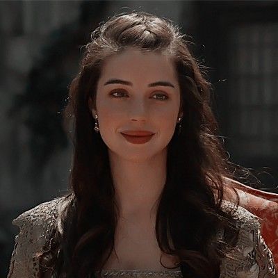 a woman with long dark hair wearing a dress and smiling at the camera while standing in front of a building