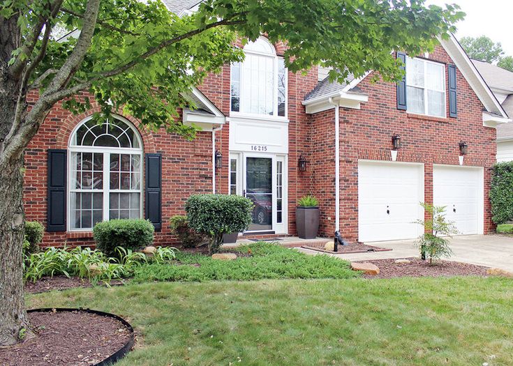 a large brick house with black shutters and white trim on the front door is surrounded by lush green grass