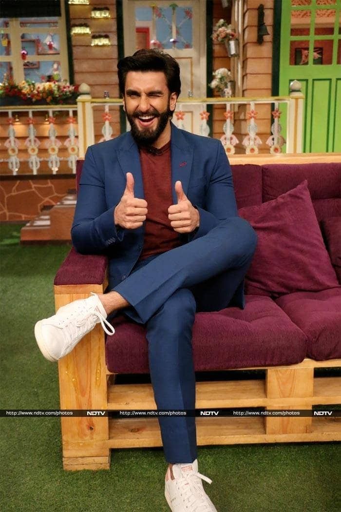 a man sitting on top of a purple couch in front of a tv screen with his thumbs up