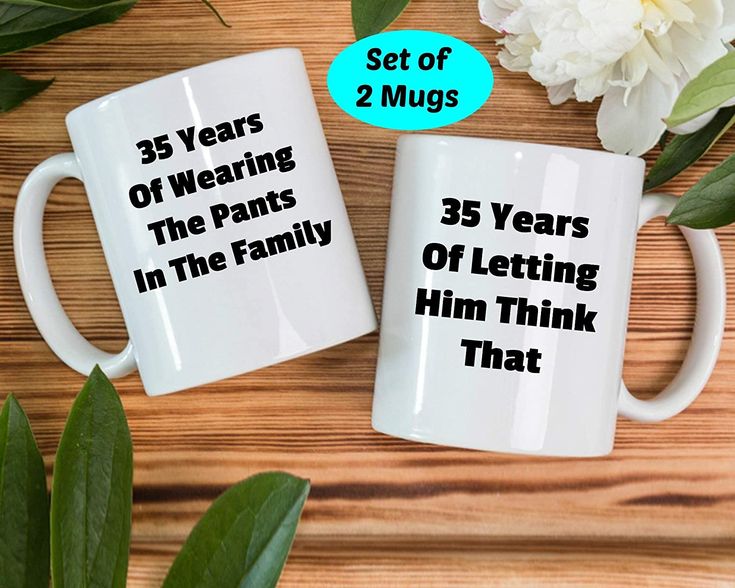 two white coffee mugs sitting on top of a wooden table next to some flowers