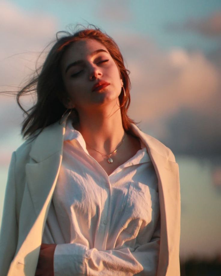 a woman with her eyes closed standing in front of the sun wearing a white shirt and blazer