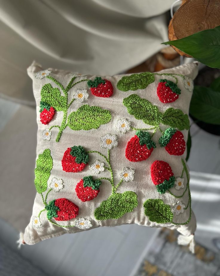 a white pillow with strawberries and daisies on the front is hanging from a hook