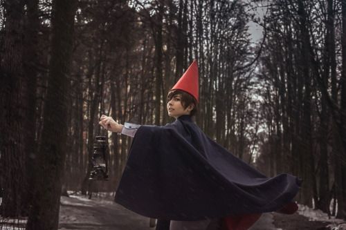 a woman wearing a cape and holding a camera in the woods