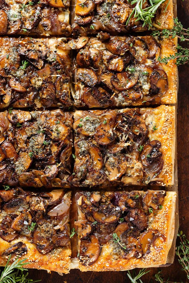 an overhead view of a pizza with mushrooms and herbs on it, cut into squares