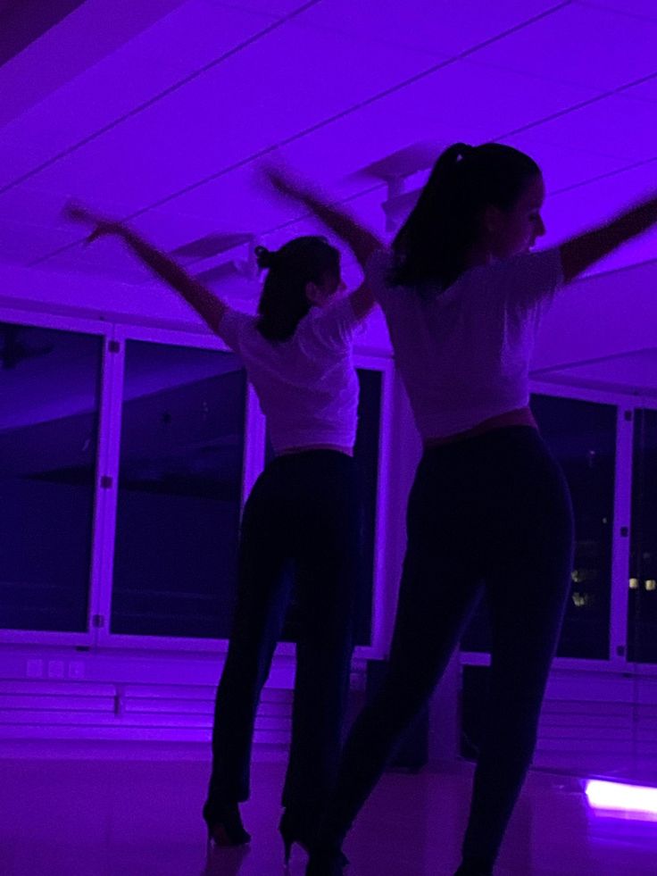 two young women are dancing in a room with purple lights on the ceiling and floor