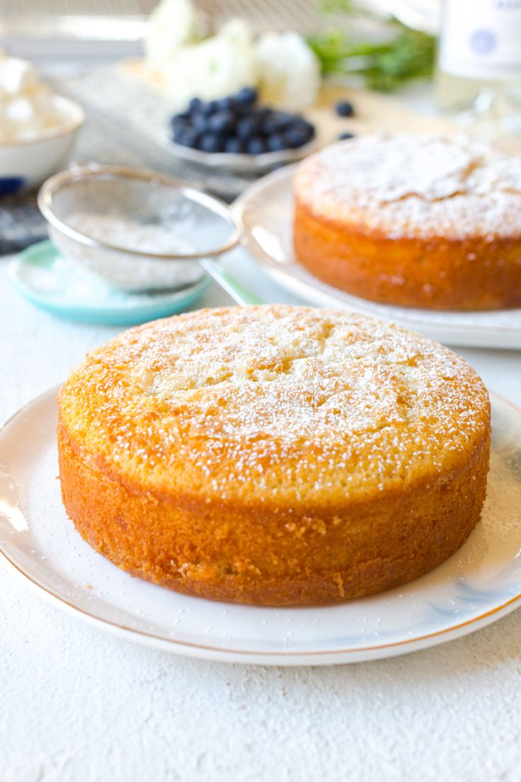 two cakes sitting on top of white plates covered in powdered sugar and blueberries