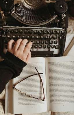 someone is typing on an old fashioned typewriter and reading a book with their hands