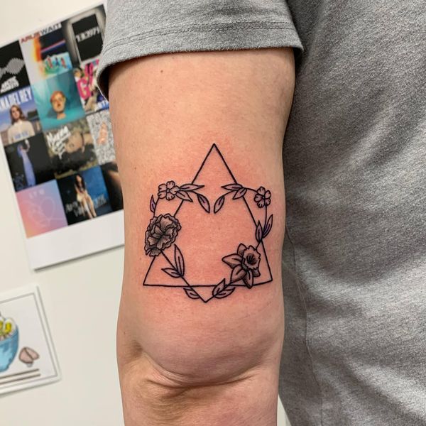 a tattoo on the arm of a man with flowers and leaves around it in a triangle