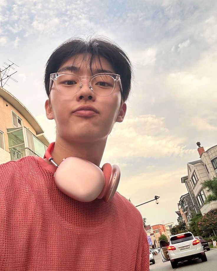 a young man wearing glasses standing in front of a building with an egg on his neck