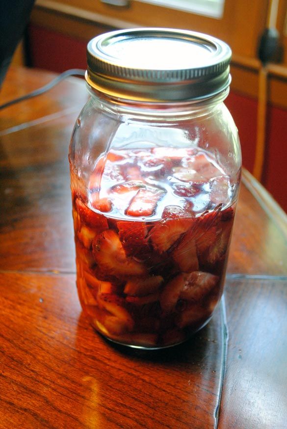 a glass jar filled with sliced strawberries on top of a wooden table