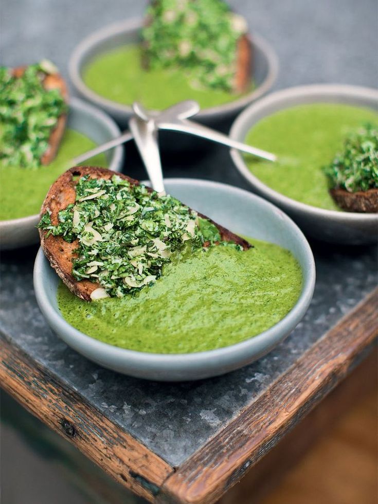 four bowls filled with green soup on top of a table