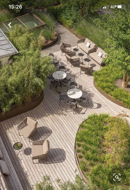 an aerial view of a wooden deck with tables and chairs, surrounded by greenery