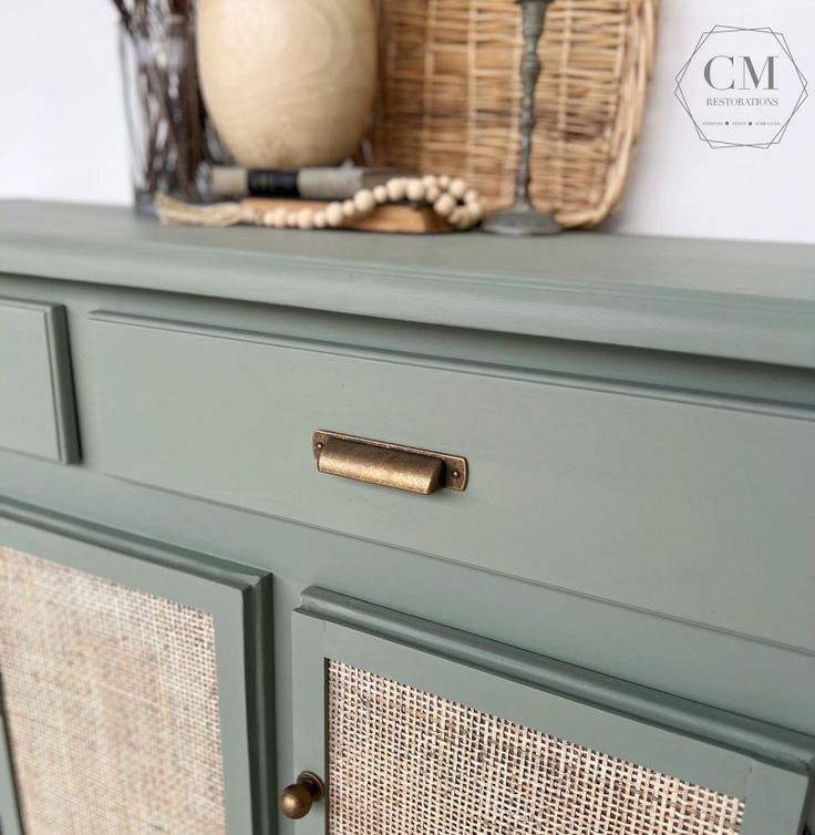 a green dresser with wicker handles and brass pulls