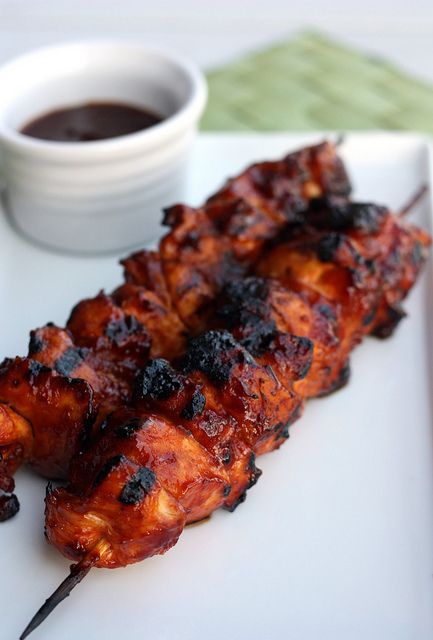 a white plate topped with chicken skewers next to a cup of sauce